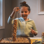 Girl holding up homemade bird feeders and smiling