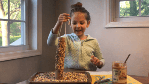 Girl holding up homemade bird feeders and smiling